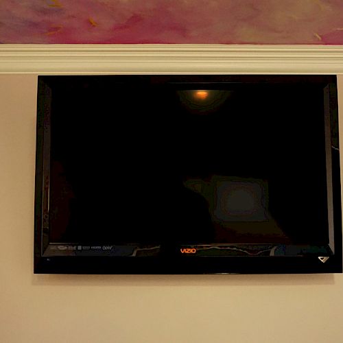 A wall-mounted flatscreen TV with a black screen is centered below a vibrant, colorful piece of artwork on the ceiling.