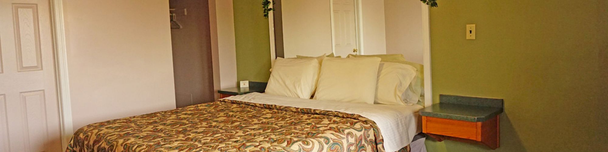 A cozy hotel room with a patterned bedspread, white pillows, wall decor above the bed, and green and beige walls, creating a warm ambiance.