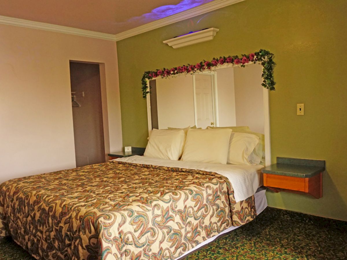 A bedroom with a bed, pillows, and floral-patterned bedspread, wall-mounted mirror, shelf, and light, and green and peach-colored walls ends the sentence.