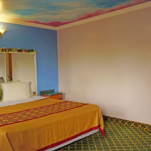 A hotel room featuring a large bed with a yellow bedspread, a blue wall with a mirror, decorative vines, and an open door to a bathroom.