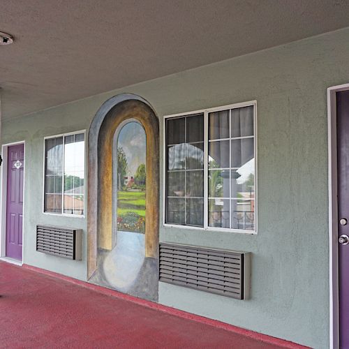 A corridor with purple doors, including door 114, two large windows, and a mural depicting an archway leading to a scenic landscape.