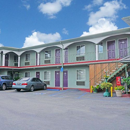 A two-story motel with an outdoor parking lot, cars parked, and staircases leading to the second-floor rooms. End of sentence.