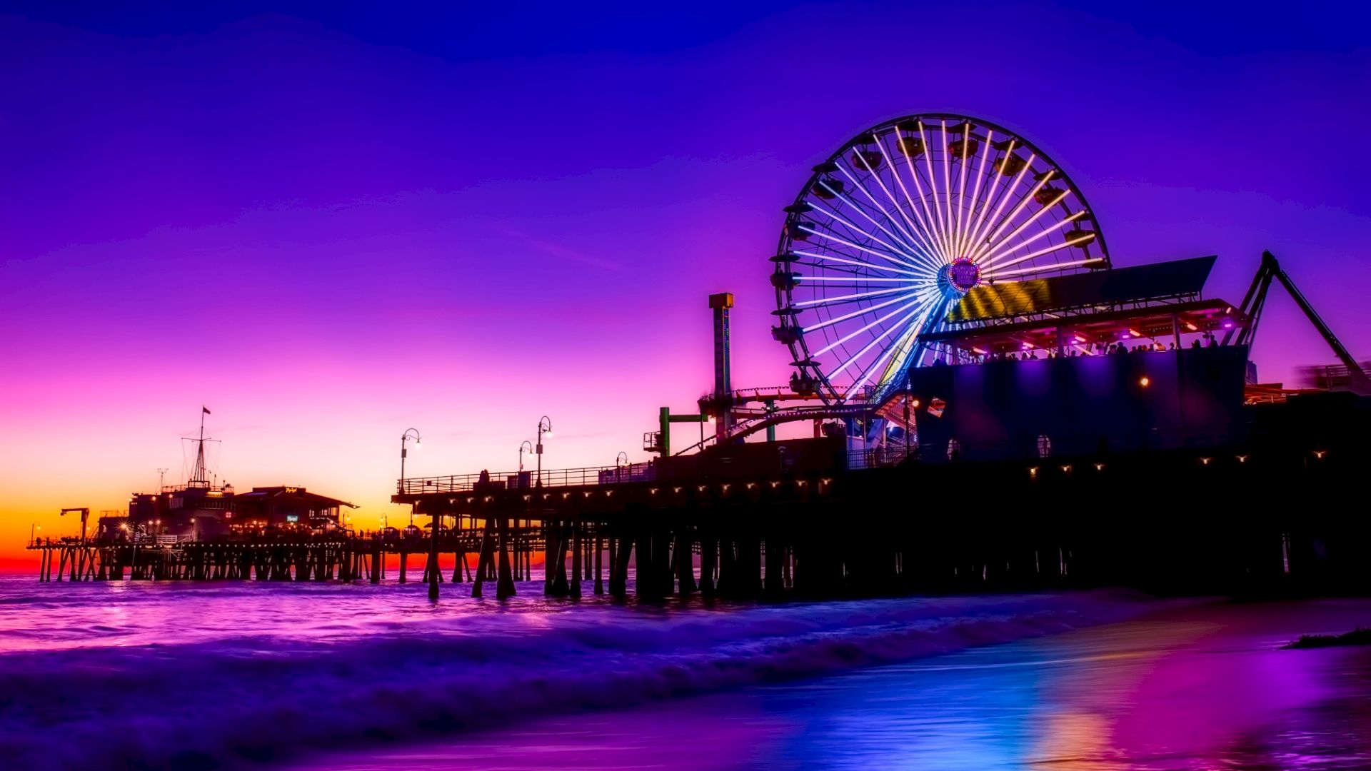 A vibrant sunset with a silhouetted pier, featuring a lit Ferris wheel and calm ocean waves in the foreground.