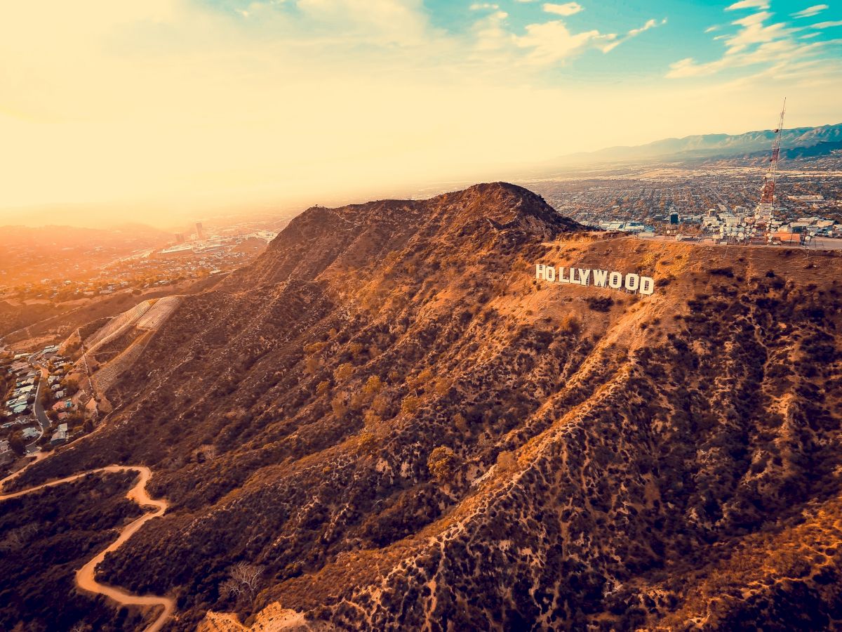 The image shows an aerial view of the Hollywood hills with the iconic Hollywood sign during sunset, overlooking the cityscape below, ending the sentence.