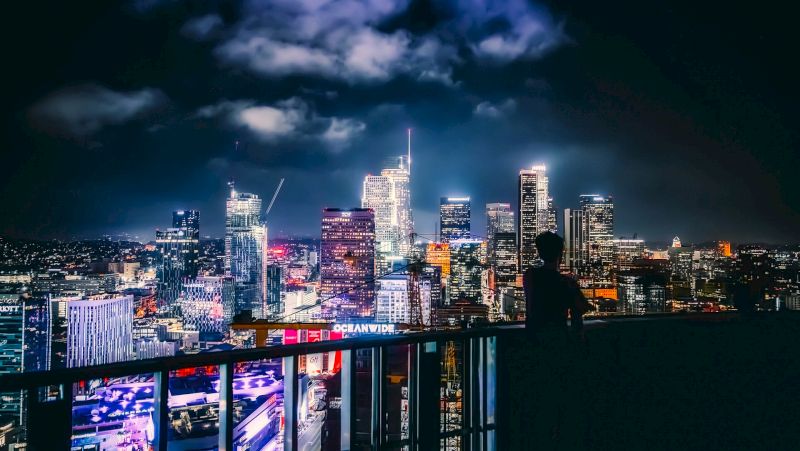 A nighttime cityscape with skyscrapers and a railing in the foreground.