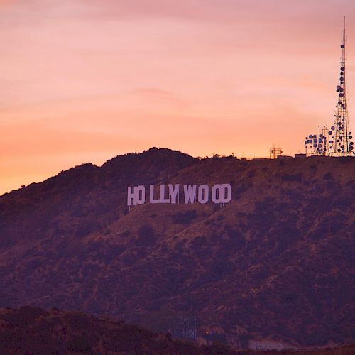 A photo of the iconic Hollywood sign on a hillside during a sunset, with a tall communication tower visible in the background.