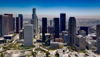 This image shows an aerial view of a cityscape with numerous skyscrapers and buildings under a clear blue sky during the day.