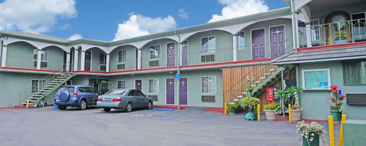 A two-story motel with a parking lot and cars parked in front of it.