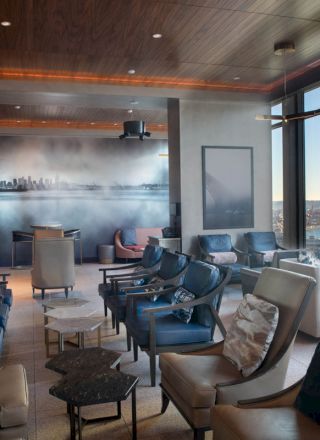 A modern lounge with comfortable seating, large windows with a scenic view, and contemporary decor including a mural of a city's skyline.