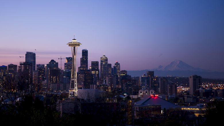 A cityscape at dusk with the Space Needle in the foreground and Mount Rainier in the background, showcasing Seattle’s iconic skyline and landmarks.